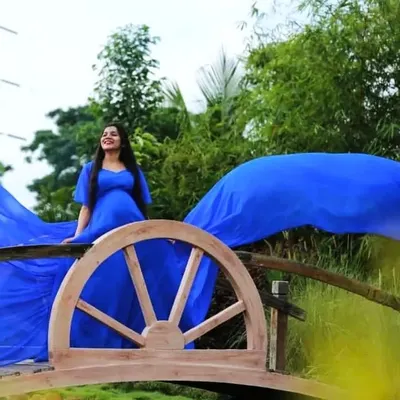 An ethereal shot of a mom-to-be on a rustic wooden bridge, surrounded by greenery. The flowing blue fabric of the gown adds a touch of magic to the natural scenery.