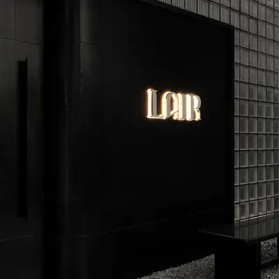 The entrance to Lair, where the brand's name glows against a monolithic black facade and a wall of glass bricks. This is the first clue in a narrative of concealment, hinting at the world that lies behind.