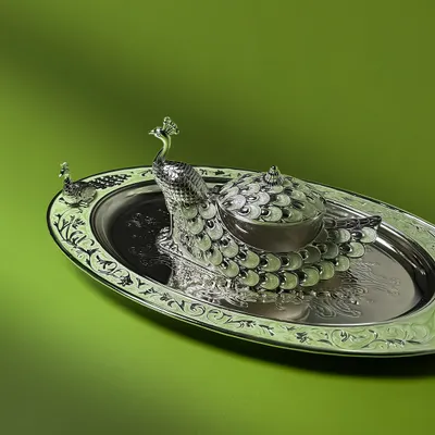The majesty of the peacock is captured in this stunning silver-plated dry fruit box and tray set. The intricate enamel work and detailed engraving make it a regal centerpiece, perfect for festive hosting or as a luxurious wedding gift.