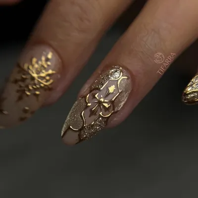 A detailed look at our 3D gold work. This almond nail extension features a hand-sculpted golden bow and filigree pattern over a sparkling cat-eye base.