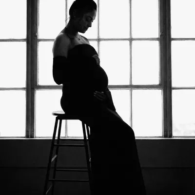 A powerful black and white silhouette of the mother-to-be. Seated on a stool against a window, this artistic shot uses shadow and light to create a moody and contemplative portrait.