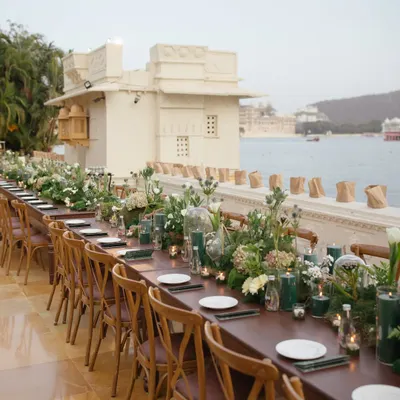A long, single-table setup for a welcome dinner by the waters of Udaipur. This layout fosters a sense of community and intimacy, allowing guests to connect.