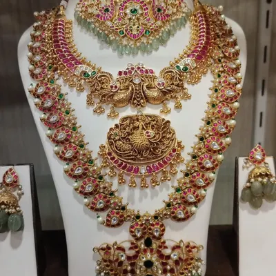 A grand Kempu bridal set with a mix of ruby, emerald, and uncut stones. This layered set includes a choker, a peacock-motif haram, and a statement pendant necklace.