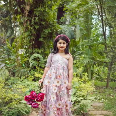 A whimsical outdoor portrait of a little girl in a beautiful floral dress, holding a basket of roses. The lush green background makes her feel like a character from a fairy tale.