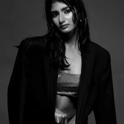 A dramatic black and white portrait of a model with the "wet look," wearing a silver top and black blazer. The high-contrast lighting creates a powerful, editorial feel.