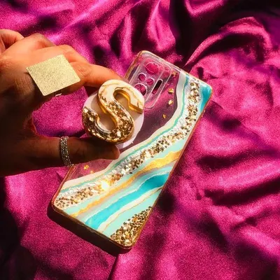 This geode-style phone case features turquoise and white resin with gold accents, paired with a matching initial pop socket. It's a glamorous and personalized accessory.