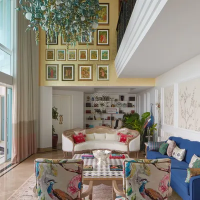 In this double-height South Bombay living room, we created multiple seating areas to make the large space feel intimate. A gallery wall draws the eye upward, while a mix of classic and modern furniture, like the floral armchairs and bold blue sofa, adds personality and color.
