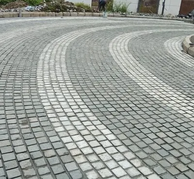 A curved driveway created with grey and white cobblestones. This pattern adds a dynamic and elegant feel to the entrance of the property.