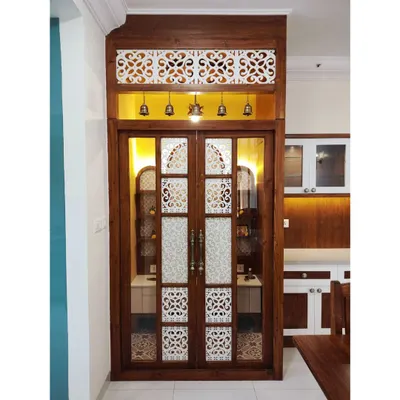 The entrance to the magnificent pooja room in #TheDivinityHome. The custom doors feature intricate jaali work, frosted glass panels, and traditional brass bells, creating a grand and welcoming threshold to this sacred space.