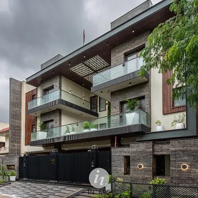 Another view of the completed residence in Greater Noida. The design uses a mix of stone cladding and wood-finished louvers to create texture and visual interest across multiple levels.