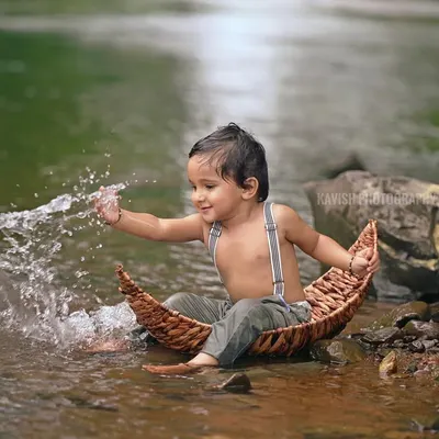 A joyful shot of a little boy splashing water while sitting in a small, rustic boat. Outdoor sessions like this allow for spontaneous and fun moments.