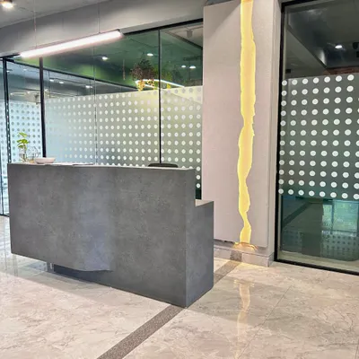 The reception area of a Gurugram corporate space, featuring a minimalist concrete-finish desk and a unique, river-like lighting feature. The design sets a clean, modern, and sophisticated tone for visitors.