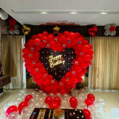 A grand romantic gesture for a birthday. This large heart-shaped balloon frame is decorated with small photos of the couple and has a "Happy Birthday" neon sign in the center, creating a beautiful and personal backdrop.
