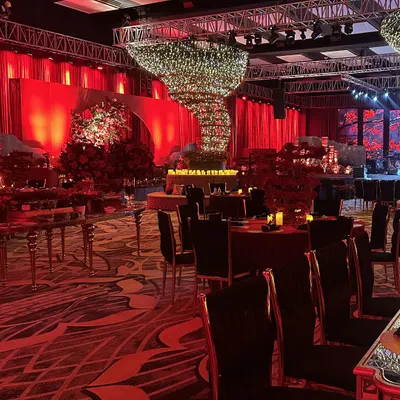 A wide shot of the sangeet at Fairmont Mumbai, bathed in a dramatic red glow. You can see the scale of the event, from the velvet-draped walls to the statement flower tornado chandelier, all working together to create an immersive world of color.
