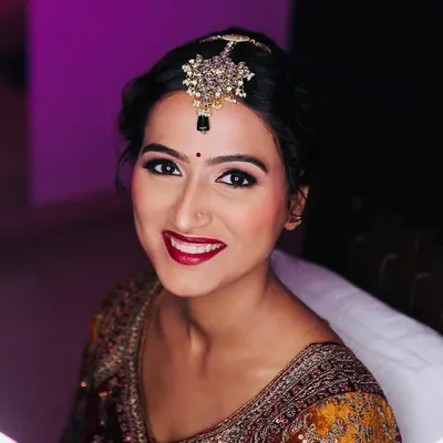 A radiant bride ready for her big day. This look features a classic red lip, defined winged eyeliner, and glowing skin, framed by a beautiful maang tikka.