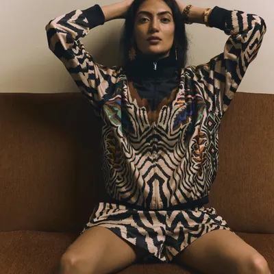 A bold, confident pose from a fashion editorial. The model's direct eye contact and powerful stance on the couch perfectly match the energy of the vibrant, animal-print outfit.