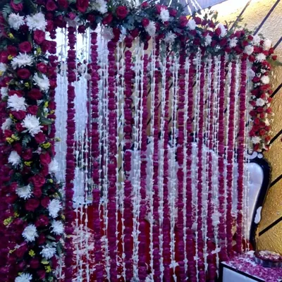 This is a beautiful first night room decoration featuring a wall of hanging flower strings. The backdrop is made of red and white flowers, creating a dense and fragrant floral curtain.
