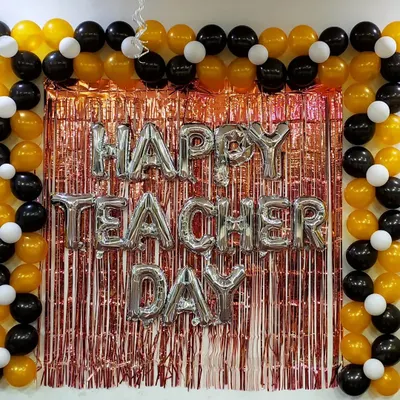A classic backdrop for an office Teacher's Day celebration. This setup features a rose gold tinsel curtain, 'Happy Teacher Day' silver foil balloons, and a neat frame of black, gold, and white balloons, creating a perfect spot for photos.