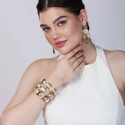 A striking close-up of a model wearing a bold, crystal-studded cuff bracelet and matching earrings. The direct gaze and clean lighting make this a powerful hero shot for a contemporary jewellery brand's homepage or ad campaign.