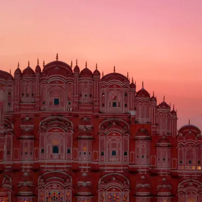 The iconic Hawa Mahal in Jaipur glows under a pink and orange sky. Capturing this landmark at sunset reveals why Jaipur is called the Pink City, a truly magical sight.