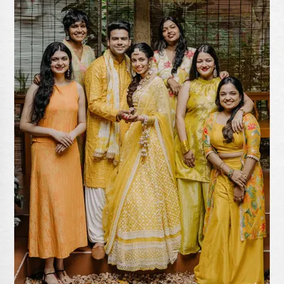 A happy group photo of the couple with their family and friends during their Haldi ceremony, all dressed in beautiful shades of yellow.