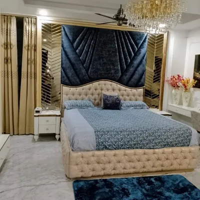 A master bedroom designed for pure luxury and comfort. The deep blue velvet headboard creates a dramatic focal point, complemented by a stunning crystal chandelier and custom mirrored panels, proving that a bedroom can be both a restful sanctuary and a statement of style.