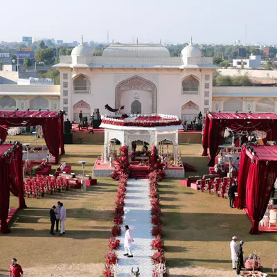 A breathtaking aerial view of the sundowner wedding setup at Anantara Jaipur. The grand scale of the palace architecture is balanced by the striking red and white decor, creating a truly royal path for the couple's ceremony.
