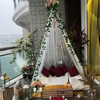 This is the daytime view of our romantic proposal teepee, set up on an apartment balcony. The sheer fabric, ivy vines, and floral accents create a beautiful and serene setting before it transforms with lights at night.