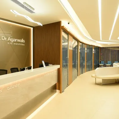 The main reception and waiting area at Dr. Agarwal’s Eye Hospital in Bangalore. The curved reception desk and flowing ceiling lights guide patient movement, while the wood and light color palette creates a welcoming atmosphere.