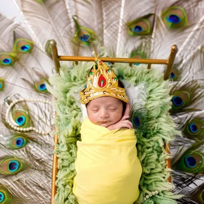 Our littlest Krishna, sleeping peacefully on a bed of peacock feathers. This stunning overhead shot is a unique and artistic way to capture your newborn during the festive season of Janmashtami.