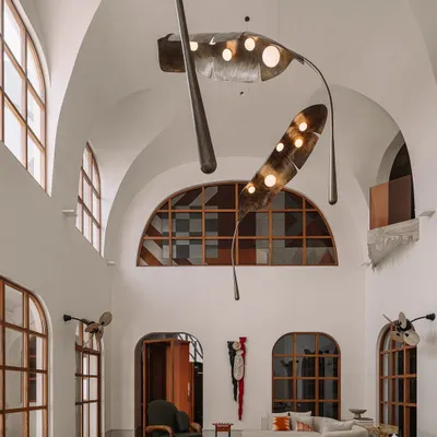Sunlight streams into the double-height living room at Rehethaan, highlighting the grand scale, arched windows, and the massive, sculptural frond-like light installation. This space was designed to feel open, airy, and connected to the outdoors.