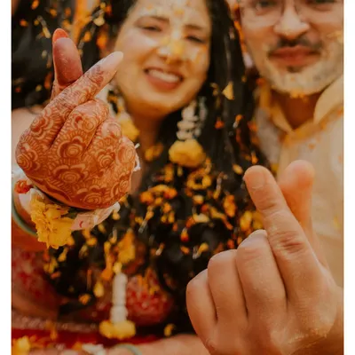 A fun, close-up shot of a couple making finger hearts during their haldi, with flower petals flying around them. This captures the playful spirit of the event.