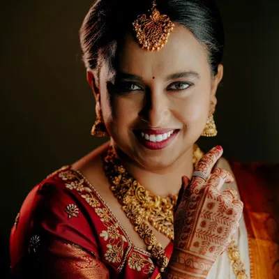 A classic, close-up bridal portrait. This shot focuses on the bride's radiant smile, detailed henna, and traditional gold jewelry.