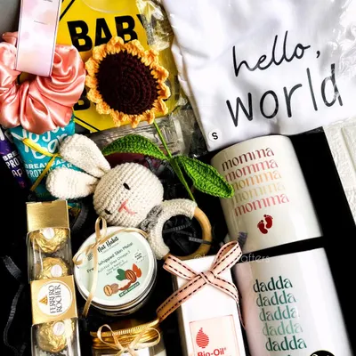 A perfect hamper for the parents-to-be, featuring 'Momma' and 'Dadda' mugs, a 'Hello World' onesie, skincare oil for the mom, and a cute crochet rattle for the baby.