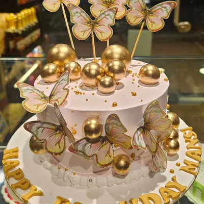 A dreamy and elegant birthday cake decorated with shimmering gold spheres and delicate wafer paper butterflies. The soft pink frosting and gold lettering create a sophisticated look.