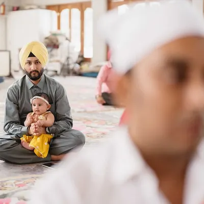 A father holds his young child during the Anand Karaj ceremony. This photo, shot with a shallow depth of field, captures a tender, multi-generational moment of faith and family.