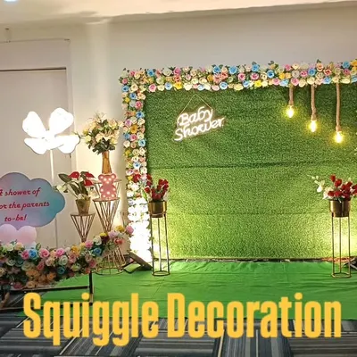 A unique and modern baby shower setup. This design features a floral crescent moon prop, a 'Baby Shower' sign, and character cutouts on an artificial grass backdrop.