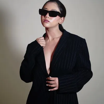 A confident pose that embodies the 'boss lady' vibe of this shoot. The simple background and focused lighting put all the attention on the model's attitude and the sharp lines of the blazer and sunglasses.