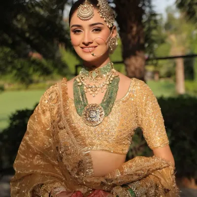 A classic bridal portrait in a shimmering gold lehenga. The look is elevated with layered emerald and polki jewelry, creating a regal contrast that is both traditional and breathtakingly beautiful.