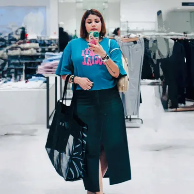 A casual shopping day look captured in a store mirror. A graphic blue tee paired with a dark denim skirt is a comfortable and cool combination for a day on your feet.