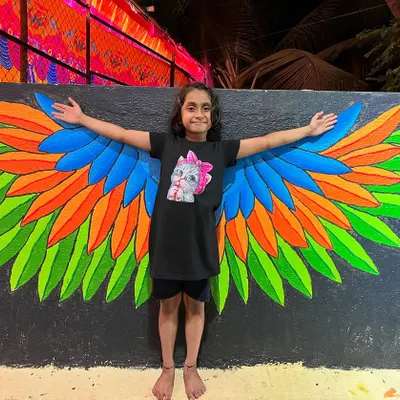 The final result: a happy visitor posing with the finished angel wing mural. My goal is to create art that people can interact and have fun with.