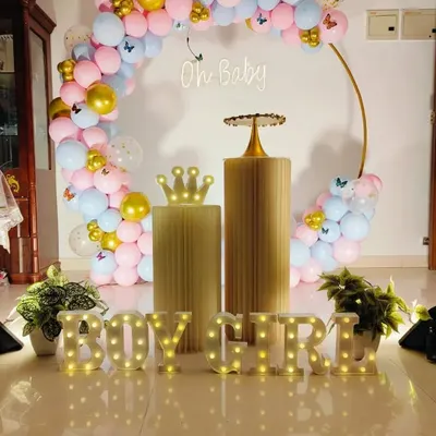 A classic gender reveal setup with a gold ring arch. The arch is decorated with pink and blue balloons, gold accents, and butterfly details, with a neon "Oh Baby" sign and "BOY or GIRL" marquee letters.