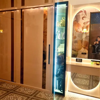 A side view of the custom closet room, showing the seamless integration of the sliding wardrobe and the vanity unit. The vertical lighting on the display cabinet adds a touch of glamour.