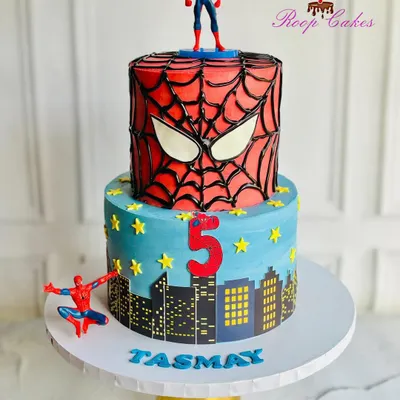 A spectacular two-tier Spider-Man cake for a 5th birthday. The top tier features the iconic mask made with piped chocolate ganache, while the bottom tier shows the city skyline, ready for some superhero action.