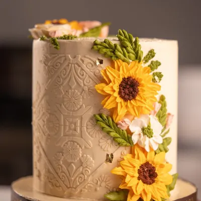An elegant custom cake featuring intricate patterns and delicate, handcrafted buttercream sunflowers. I create these bespoke designs to make your celebrations truly beautiful and unique.