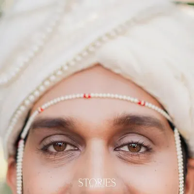 A close-up portrait of the groom on his wedding day. The focus on his expressive brown eyes and the traditional 'mundavalya' creates a simple yet powerful image.