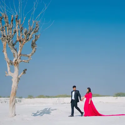 A stunning wide-angle shot of a couple walking through a vast, white landscape, the bride's red gown creating a dramatic pop of color against the minimalist background.