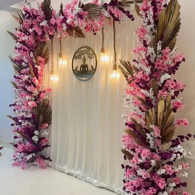 For a modern Jain ceremony, I designed this tranquil backdrop. It features a cascade of pink and white cherry blossoms over a clean white curtain, with warm Edison bulbs and a central laser-cut emblem to create a peaceful and spiritual ambiance.