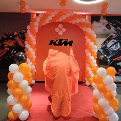 This setup for a KTM motorcycle launch features a balloon arch and pillars designed with the company's signature orange, white, and black brand colors. The decor builds excitement and draws attention to the new product reveal in the showroom.