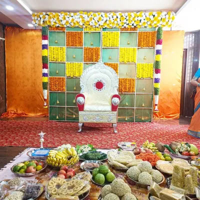 A vibrant Shreemantha setup featuring a checkered backdrop of fresh marigold flowers and an ornate silver chair for the mother-to-be, with traditional offerings displayed in front.